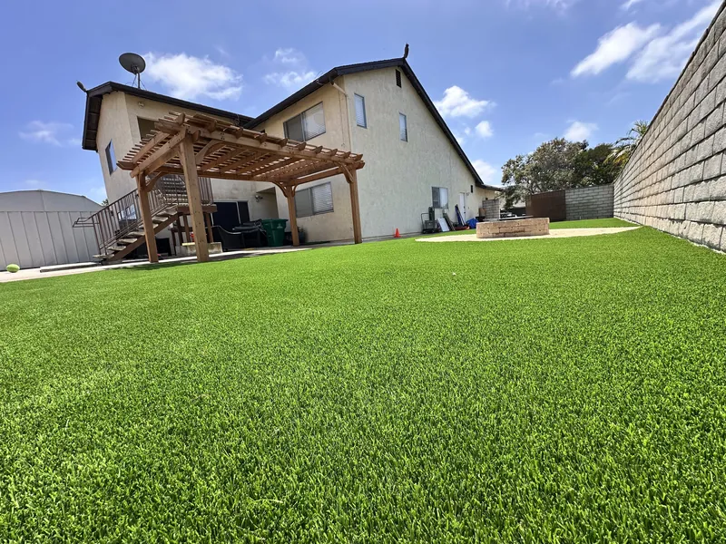 Lush artificial grass backyard lawn with wood pergola and blue sky at a San Diego County home