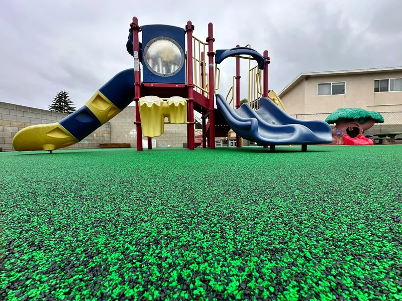 Bright green poured-in-place rubber playground safety surface under a colorful slide play structure in San Diego County, CA